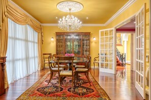 Une salle à manger avec une table ronde, des chaises, un lustre, une vitrine et un tapis à motifs.