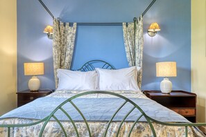 Un lit avec un cadre en métal, deux tables de chevet avec des lampes et des rideaux sur un mur bleu.