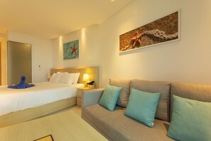 A hotel room with a bed, a sofa, a nightstand, and wall art. - Sea View Beach Bar Beach Front c114 (Rawai)
