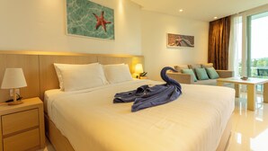 A hotel room with a large bed, a nightstand with a lamp, a seating area with a sofa and armchairs, and artwork on the walls. - Sea View Beach Bar Beach Front c114 (Rawai)