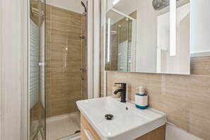 Bathroom features a glass-enclosed shower and a single sink with a soap dispenser.