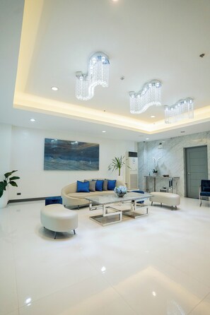 A modern living room with a beige sofa, a round ottoman, a glass coffee table, and a marble fireplace. - Stacia Hotel (Cebu City)