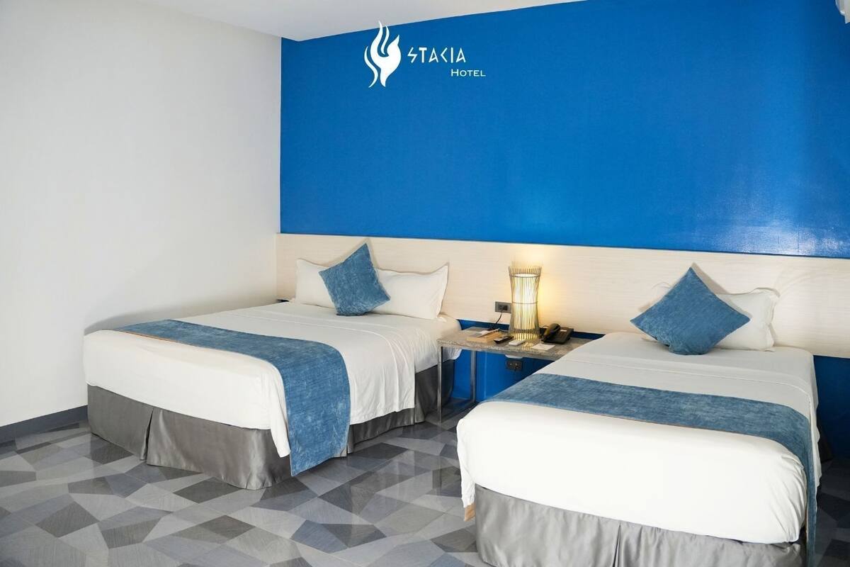A hotel room with two beds, a nightstand, and a blue accent wall.