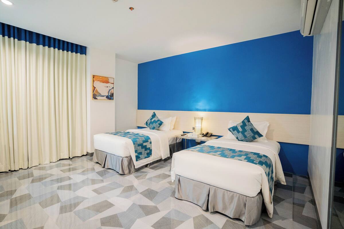 A hotel room with two beds, a nightstand, and a wall with a blue accent.