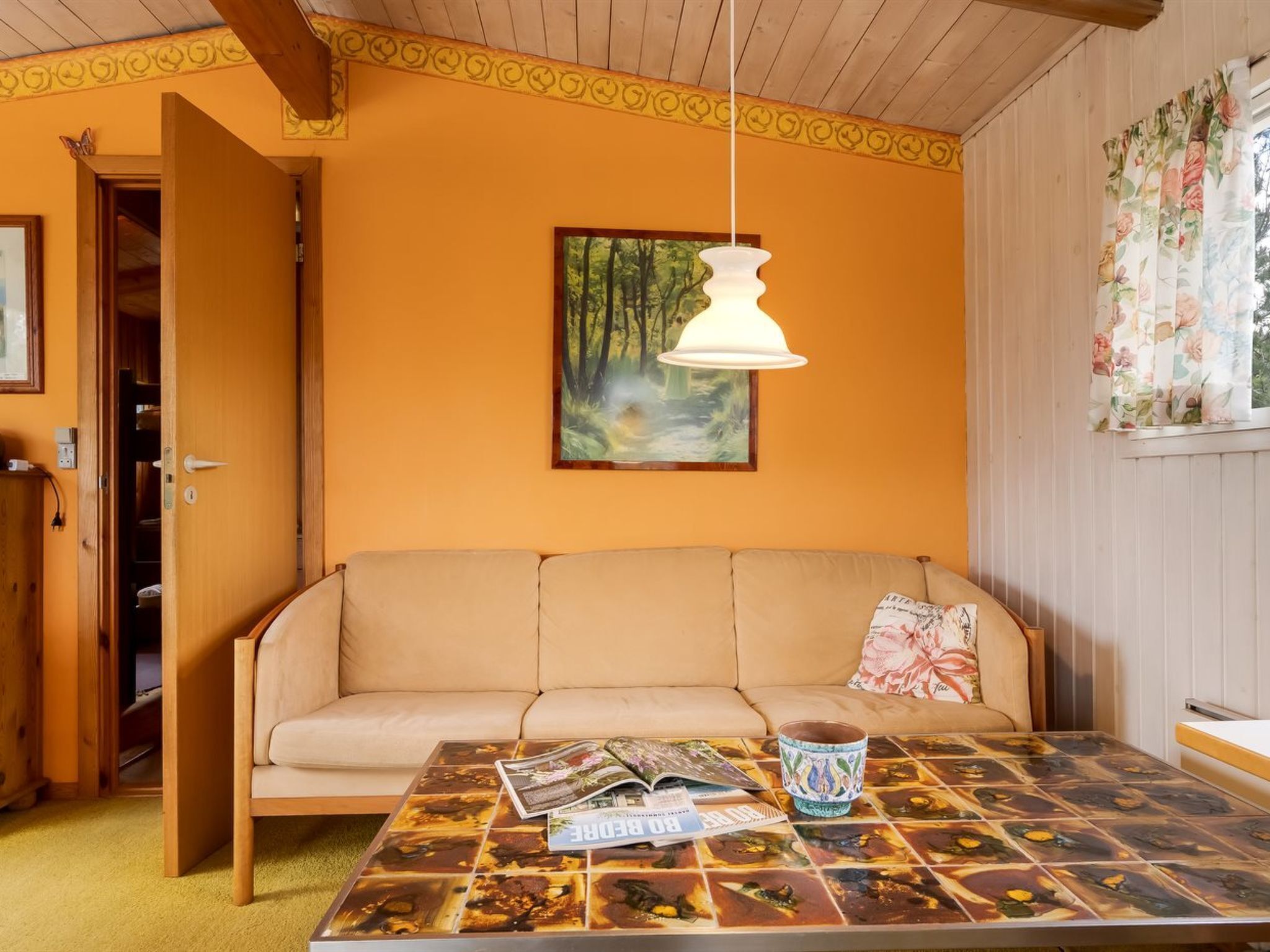 A cozy room with a beige sofa, a patterned coffee table, and a painting of a forest.