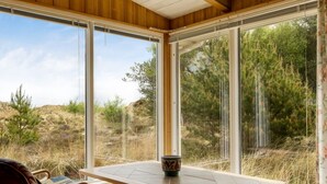 Une pièce au décor intérieur en bois, une table dont le plateau est orné de motifs, et une vue sur un paysage naturel grâce à de grandes fenêtres.