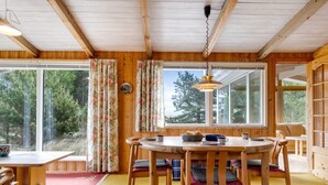 Un intérieur en bois avec une table à manger ronde et des chaises, de grandes fenêtres et une vue sur les arbres.