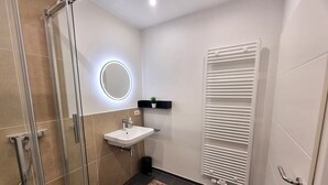 Un baño moderno con cabina de ducha de vidrio, un lavamanos blanco con espejo, un perchero y un radiador.