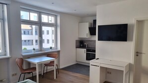 Una habitación compacta y moderna con cama, escritorio y kitchenette.