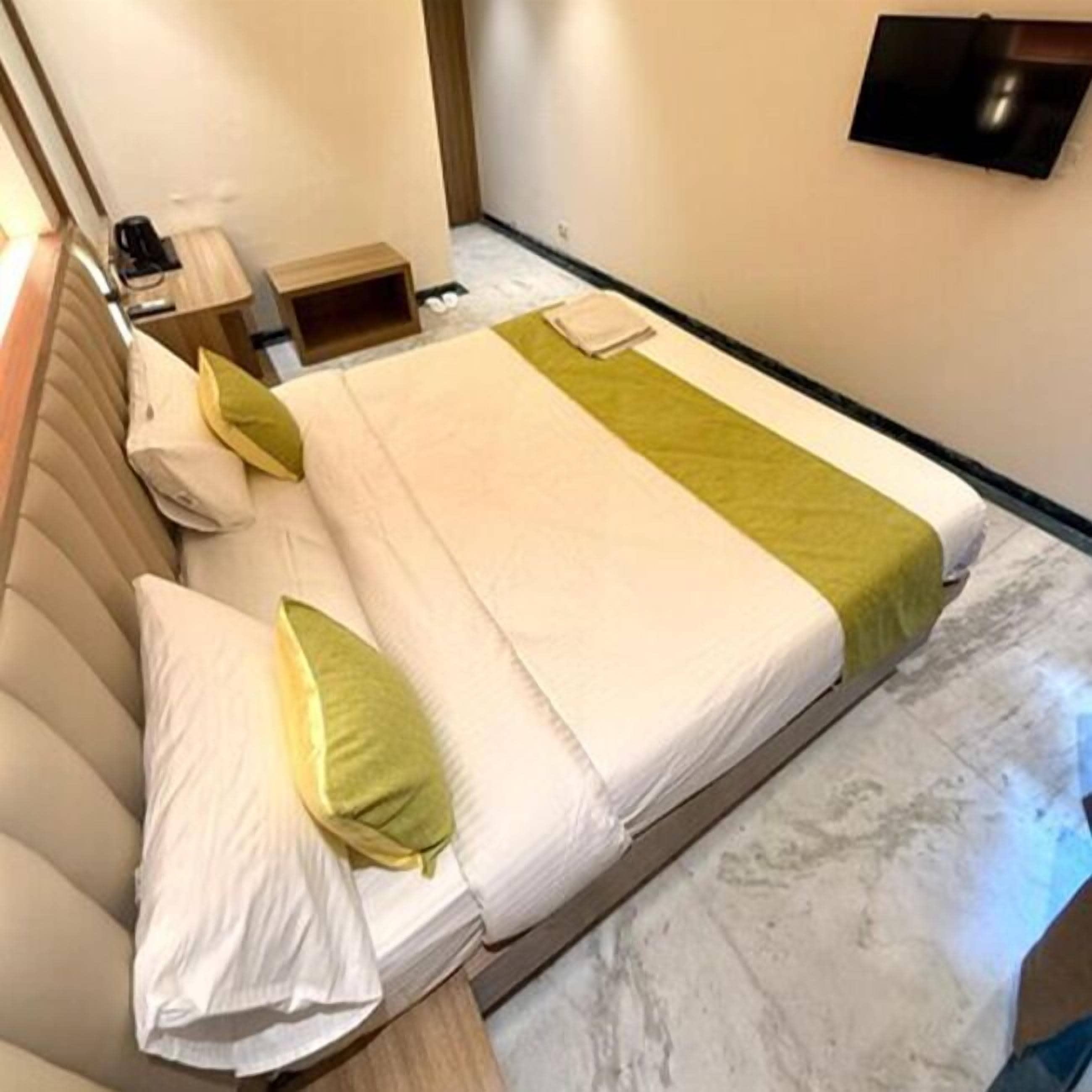 Una habitación de hotel con una cama, un televisor montado en la pared y una mesita de noche con lámpara.