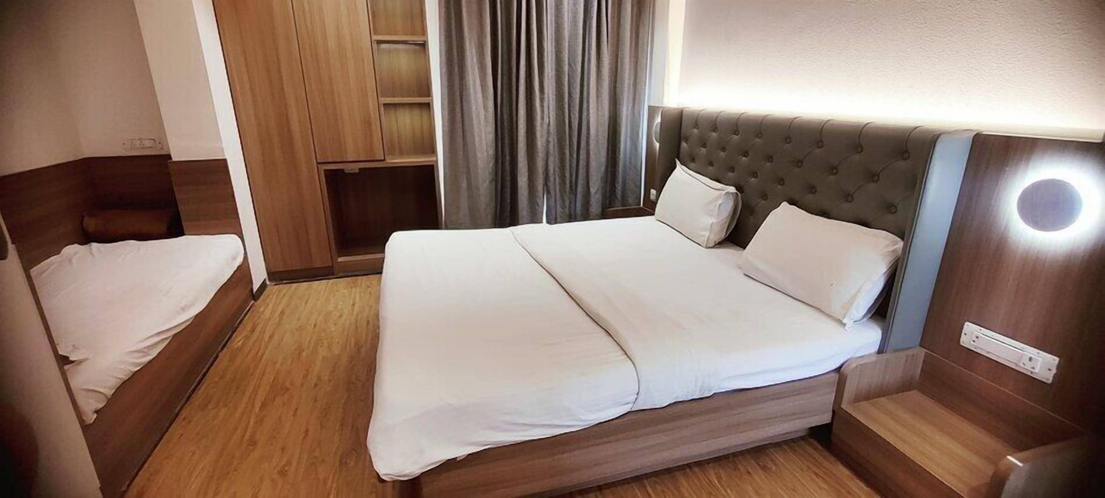 Habitación de hotel con una cama grande, una cama más pequeña, un armario de madera y una mesita de noche con una lámpara.