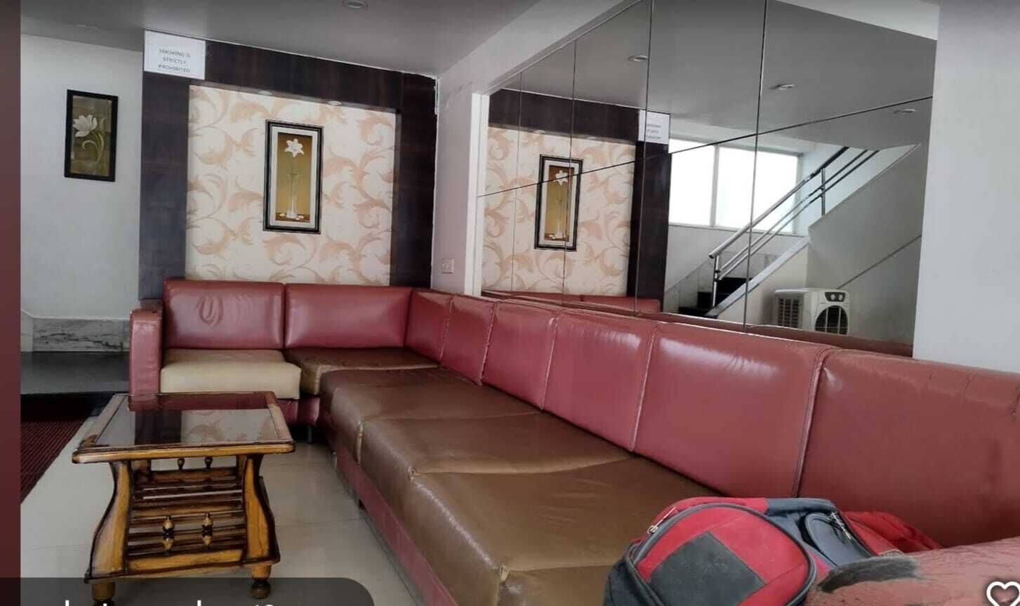 Un moderno vestíbulo de hotel con un sofá de cuero rojo, una mesa de centro de madera y un espejo grande que refleja el espacio.