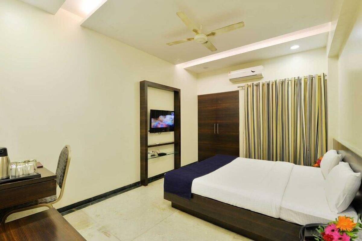 A hotel room with a bed, a desk with a chair, a television, a wardrobe, and a curtain.