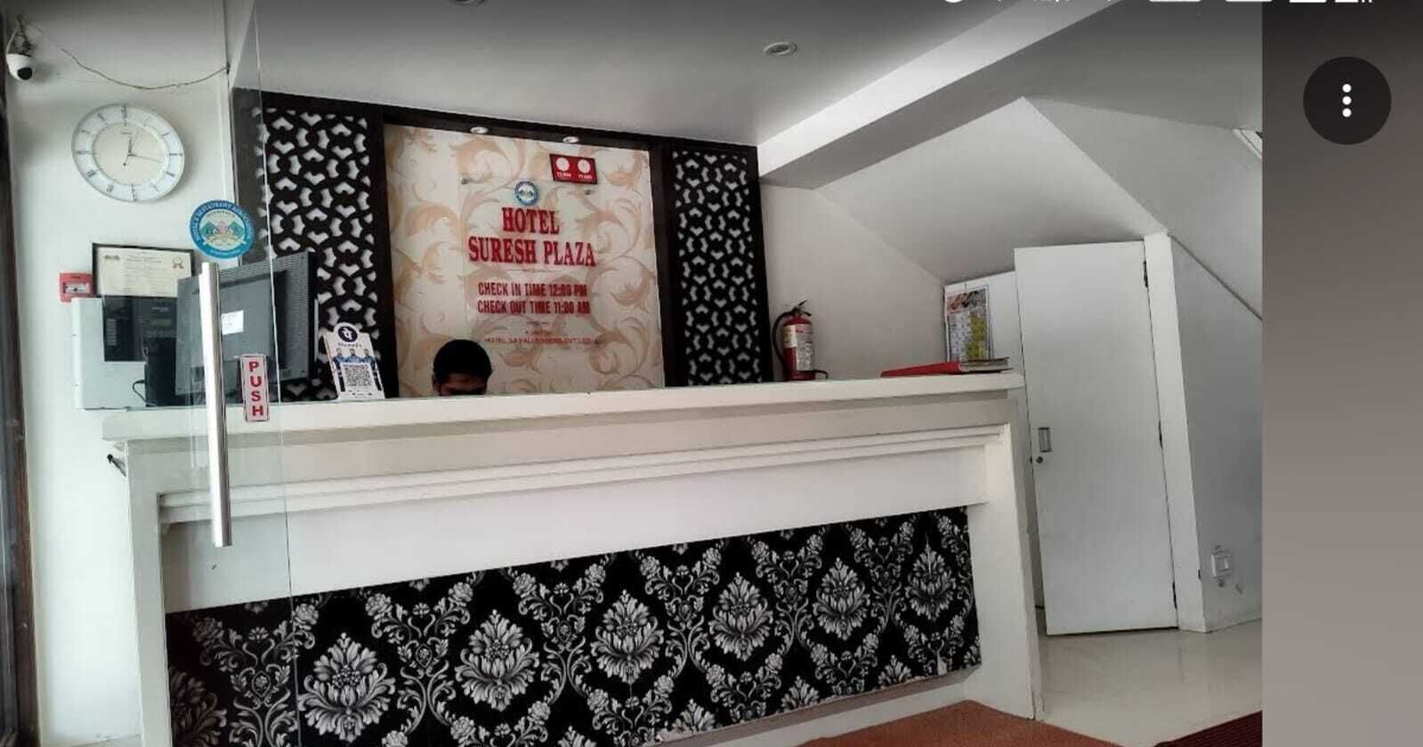 A reception area with a clock, a check-in counter, a fire extinguisher, and a patterned wall.