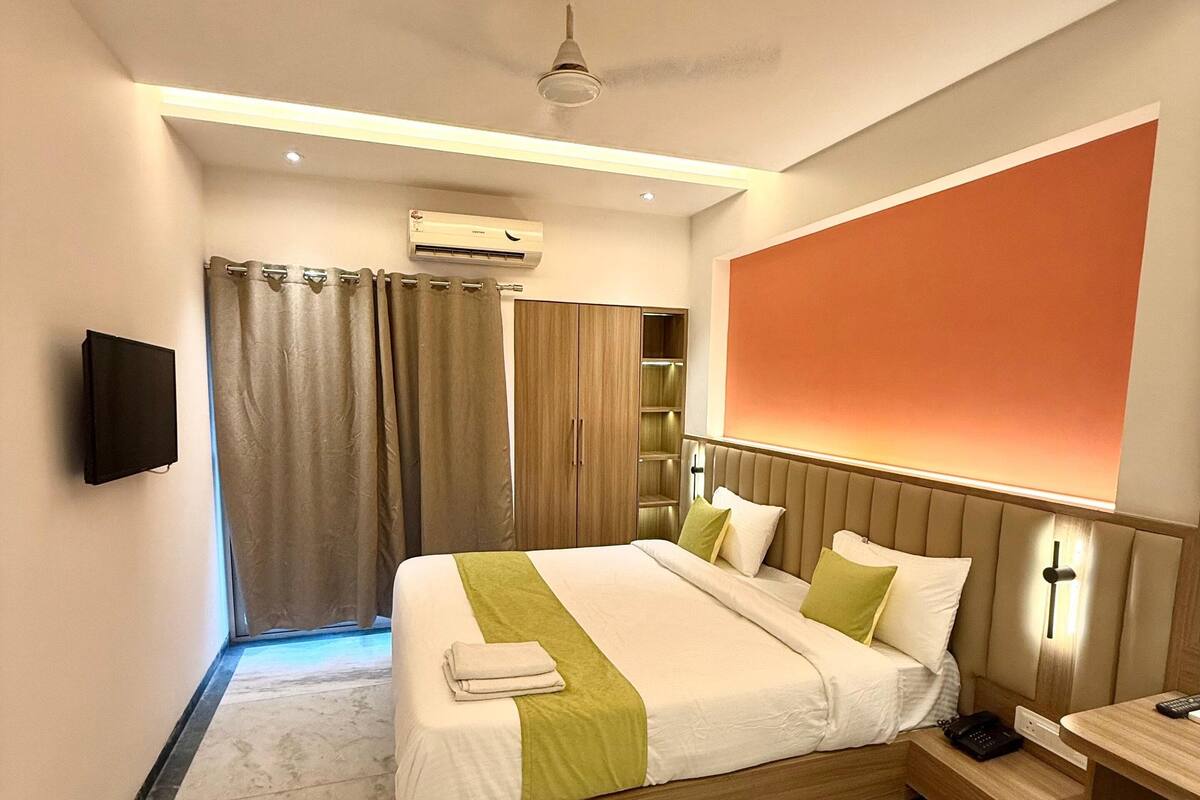 A hotel room with a bed, bedside table, and a TV mounted on the wall.