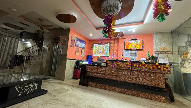 A reception area with a marble staircase, a reception desk with a patterned backdrop, and a television screen. - Hotel M A International (New Delhi)