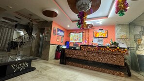 A reception area with a marble staircase, a reception desk with a patterned backdrop, and a television screen. - Hotel M A International (New Delhi)