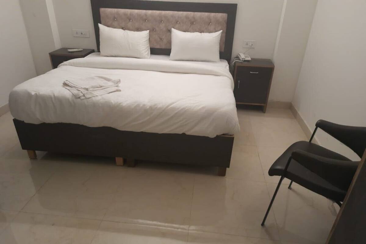 A neatly made bed with white linens, a wooden headboard, and a bedside table with a phone.