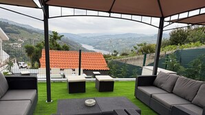 An outdoor patio with wicker furniture, a view of a river and hills, and a covered area with a roof. - Casa Pinto Douro, your vacation home with a breathtaking view.  (Baiao)