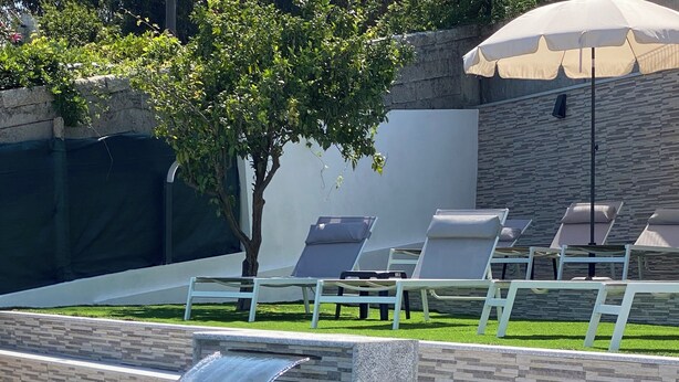 A swimming pool with a waterfall feature, surrounded by lounge chairs and a stone wall. - Casa Pinto Douro, your vacation home with a breathtaking view.  (Baiao)