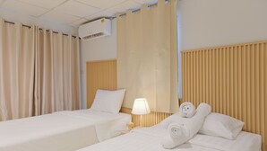 A hotel room with two beds, beige curtains, a wooden headboard, a lamp, and a towel with a bear design. - Baan Chinnakarn (Chiang Mai)