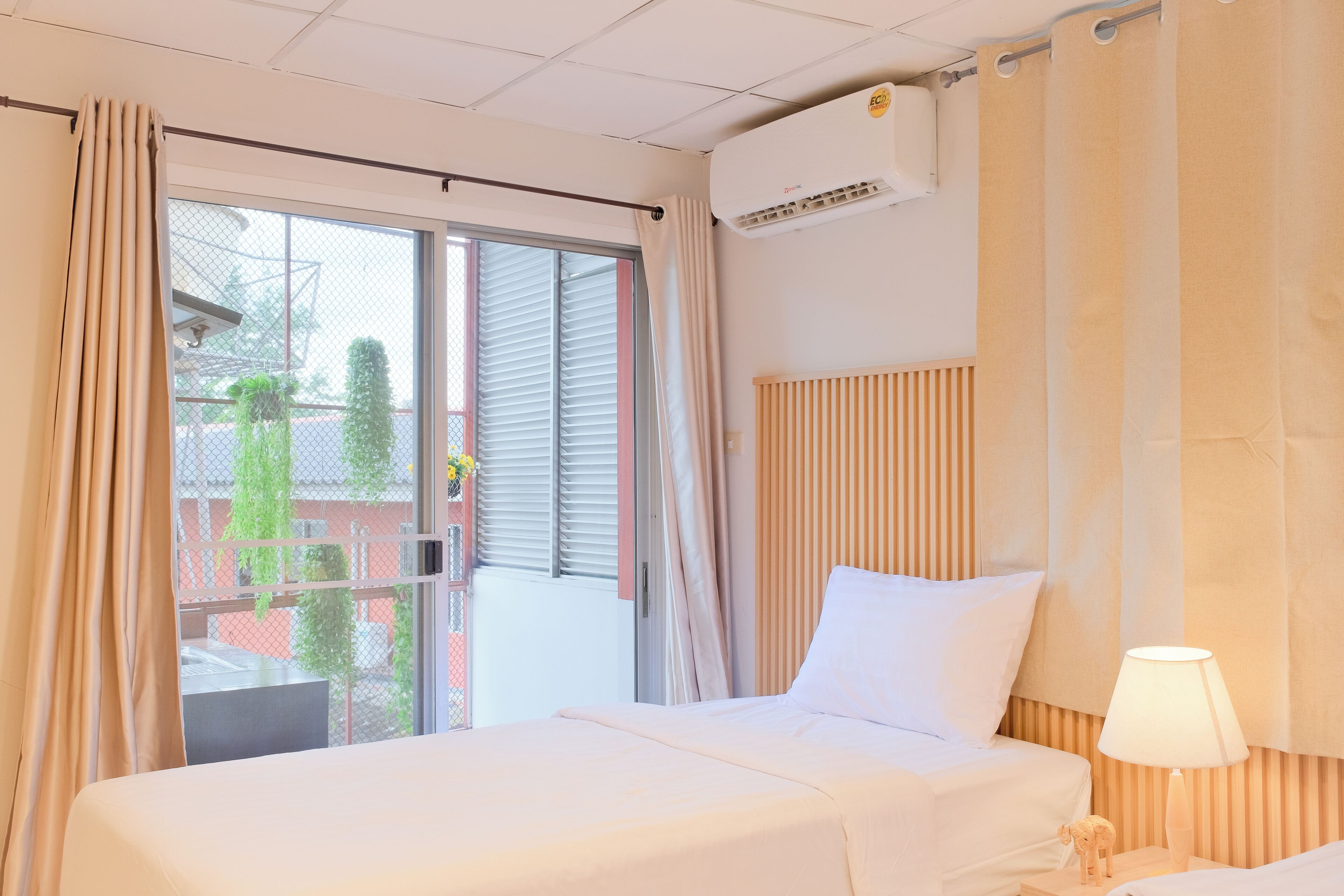 Habitació d'hotel amb un llit, una tauleta de nit, una làmpada, un aparell d'aire condicionat i una finestra amb cortines.