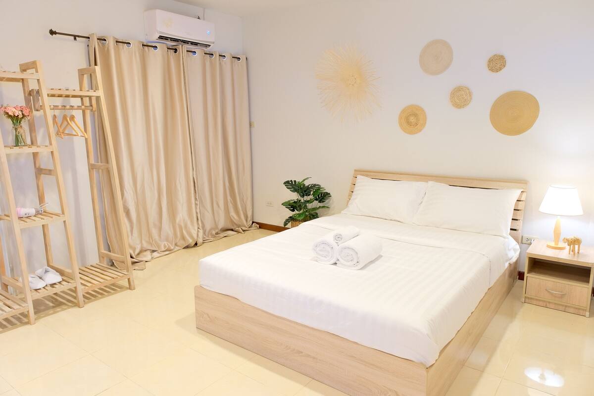 A neatly arranged bedroom with a bed, a bedside table, a lamp, and a wall-mounted air conditioner.