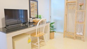 A room with a flat-screen TV, a white chair, a small table with a basket, a mirror, a potted plant, and a wooden shoe rack with shoes and a vase of flowers. - Baan Chinnakarn (Chiang Mai)