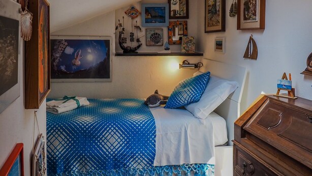 A bedroom with a bed, a dresser, and a wall with various framed pictures and decorations.