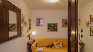 Una habitación acogedora con un sofá amarillo, una mesita con una lámpara y varias obras de arte enmarcadas en las paredes.