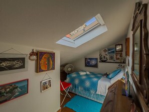 A bedroom with a skylight, a bed with a blue and white patterned bedspread, a red chair, and various wall art.
