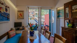 A dining area with a wooden table, chairs, a blue sofa, a vase with flowers, and a view through a glass door.
