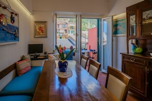 A dining area with a wooden table, chairs, a blue sofa, a vase with flowers, and a view through a glass door.