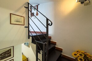 Un escalier doté d’une main courante noire et d’une balustrade en bois, menant à un palier où se trouvent un tableau encadré et un vase rempli de tournesols.