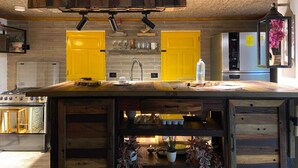 Una cocina con una isla central, gabinetes amarillos, un refrigerador de acero inoxidable y un colgante de luz.