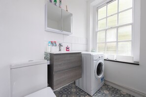 A compact laundry room with a washing machine, a drying rack, and a cabinet above the sink. - Quiet location in Central London, near Paddington, Regent Park, Lord's Cricket (London)