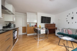 A modern kitchen with white cabinets, a dining area with a table set for two, and a living room with a sofa and a coffee table. - Quiet location in Central London, near Paddington, Regent Park, Lord's Cricket (London)