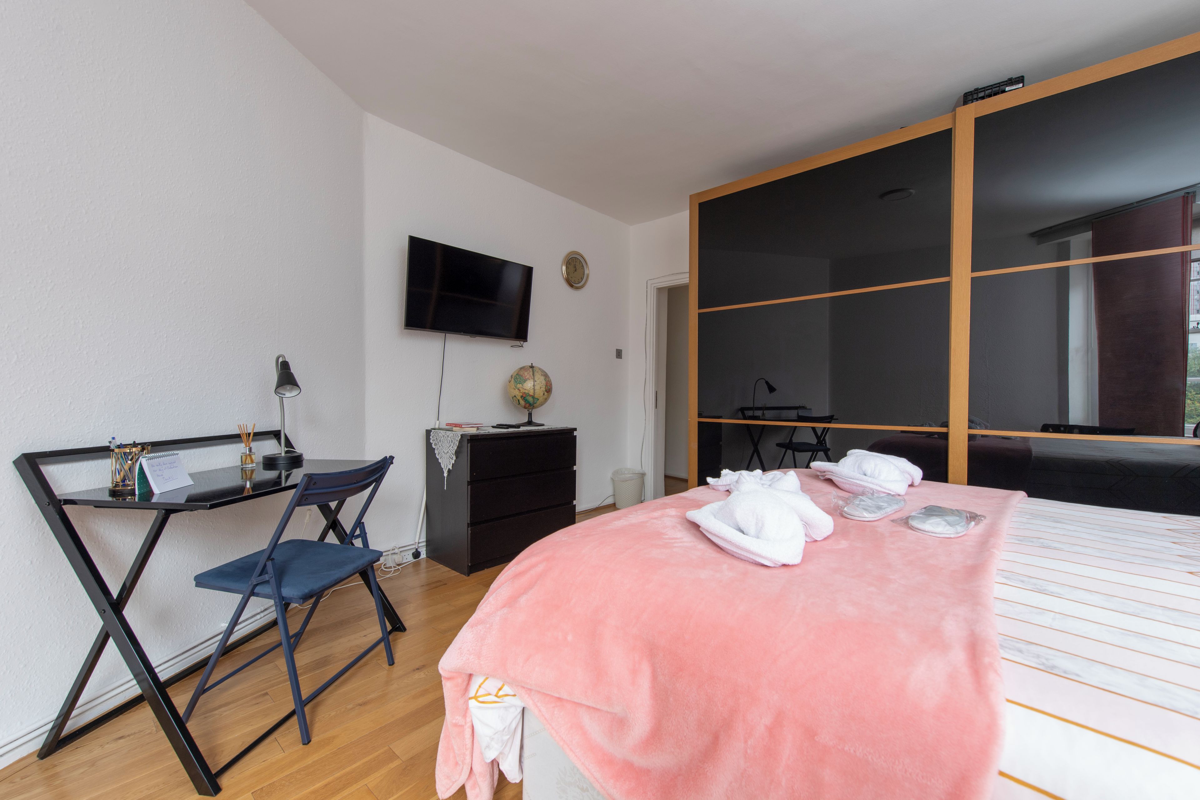 Un dormitorio con cama, un escritorio con silla, un televisor, un globo terráqueo y un armario.
