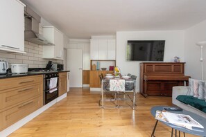 A modern kitchen with wooden cabinets, a dining area with a table set for two, and a living area with a sofa and a coffee table. - Quiet location in Central London, near Paddington, Regent Park, Lord's Cricket (London)