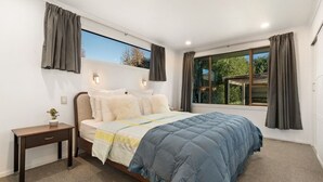 A bedroom with a bed, bedside table, and a window with curtains. - Large, spacious home great for large numbers (Cromwell)