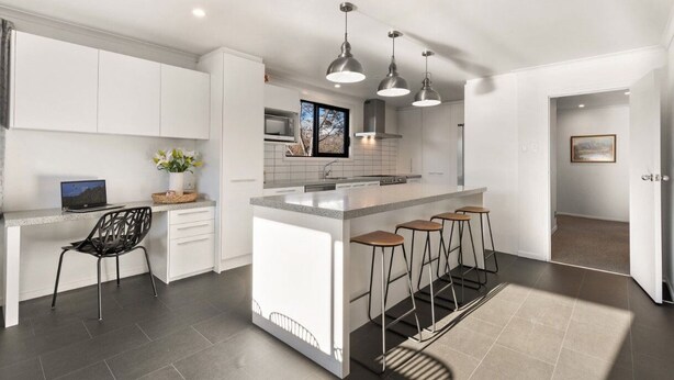 A modern kitchen with white cabinetry, a central island with stools, pendant lighting, and a view of the outdoors through a window. - Large, spacious home great for large numbers (Cromwell)