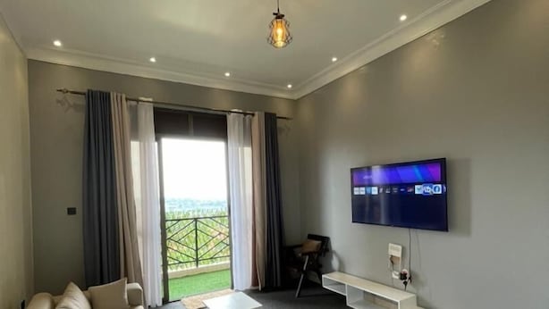 Un saló modern amb un sofà gran, un televisió de pantalla plana penjada a la paret i un balcó amb cortines.