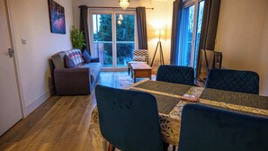 A living room with a sofa, a dining table with chairs, a floor lamp, and a view through a glass door to the outside. - Convenient 2 Bedroom Apartment in Crawley (Crawley)