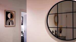 A hallway with a framed abstract artwork, a round mirror with a black frame, and a door leading to another room. - Convenient 2 Bedroom Apartment in Crawley (Crawley)