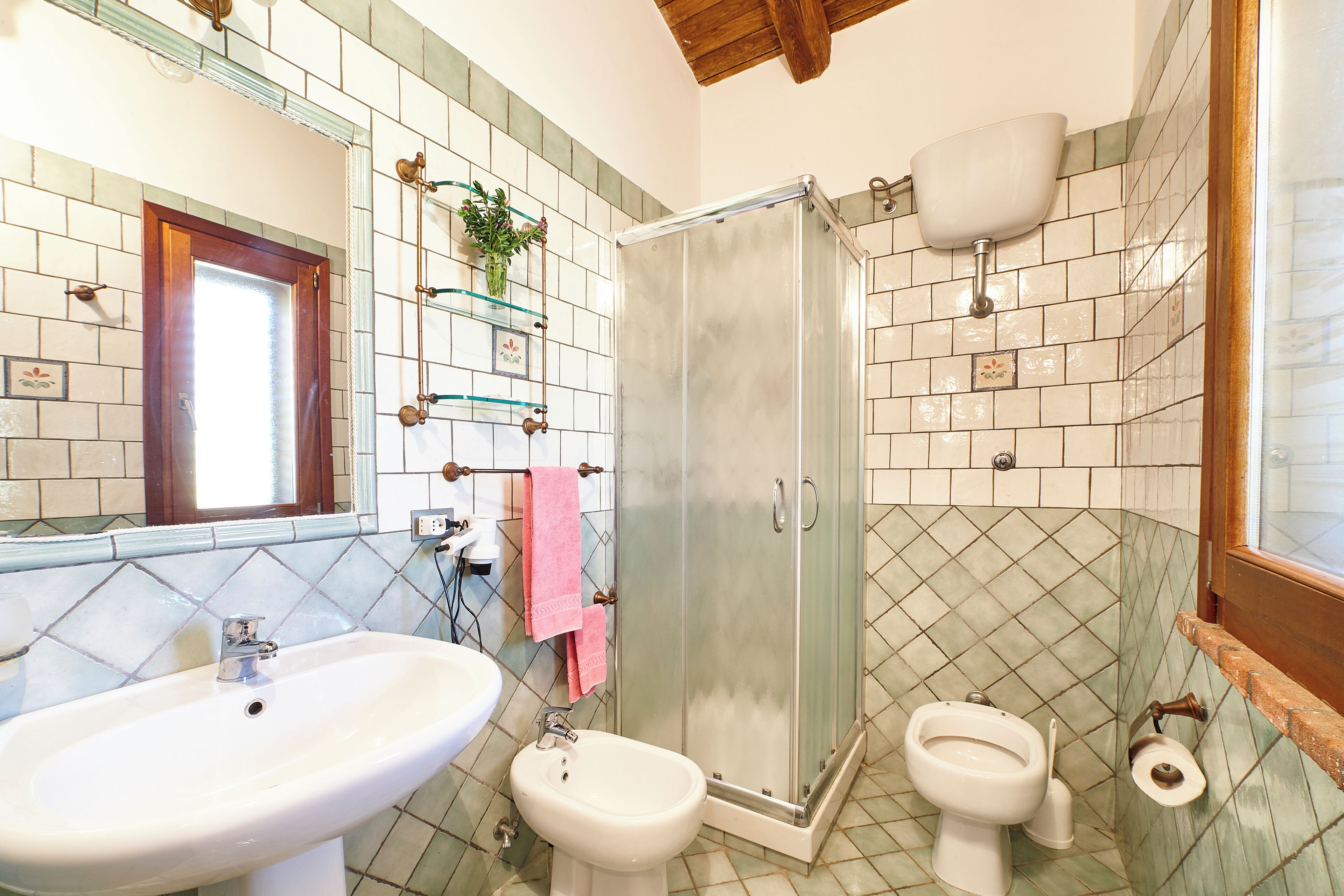 Un baño con lavamanos, bidé, inodoro y ducha con mampara de vidrio.