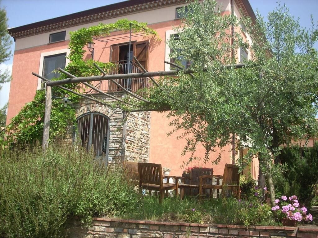 Un bâtiment à la façade en pierre, doté d’un balcon avec des rampes en métal et d’un espace jardin aménagé avec des chaises et une table.