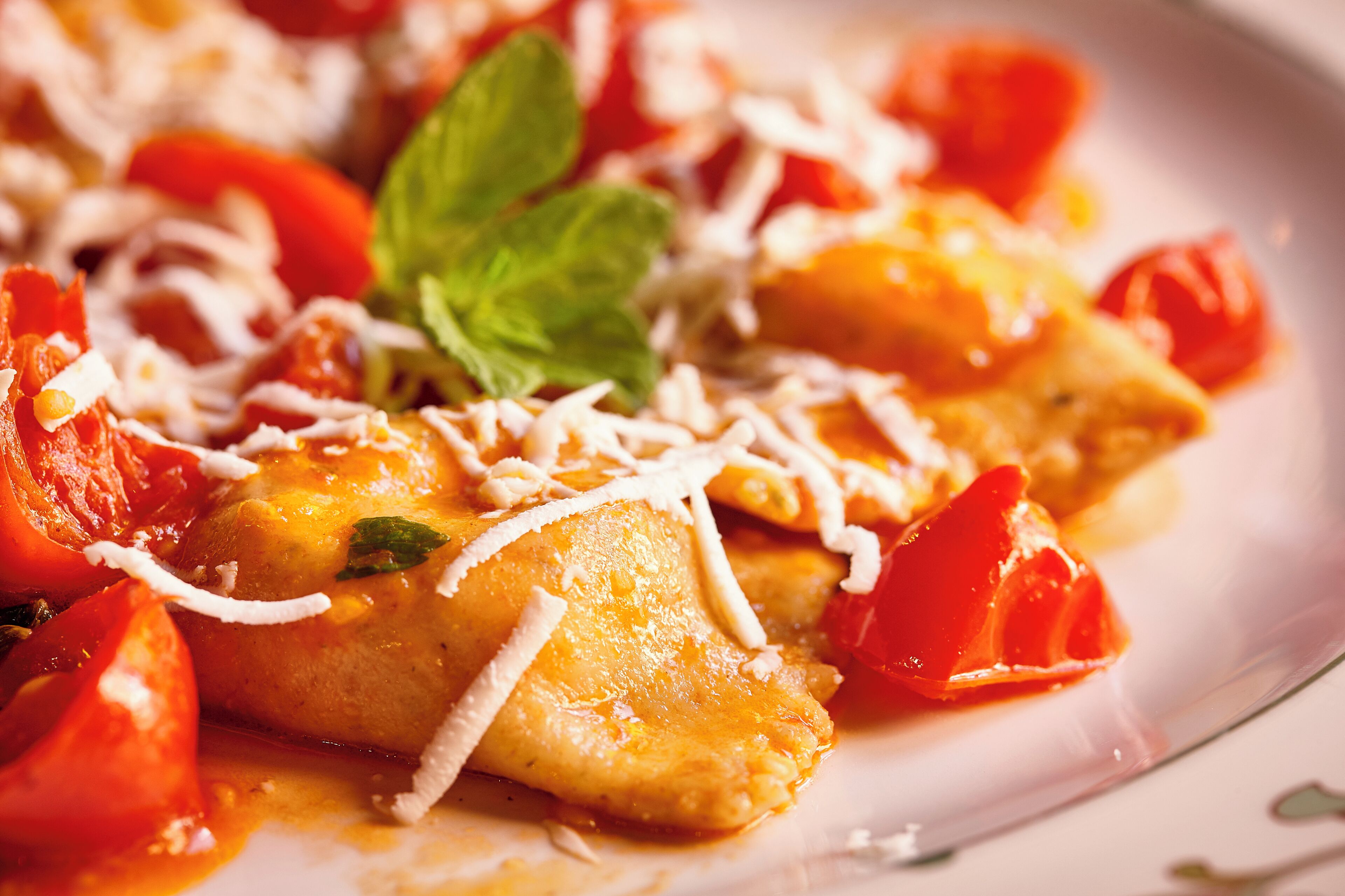 Een bord ravioli met tomatensaus en geraspte kaas.
