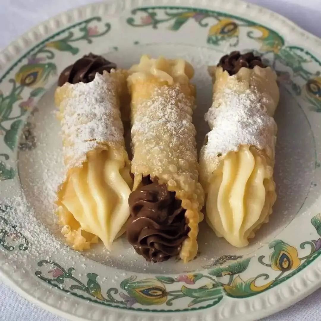 Three chocolate-filled cannoli on a decorative plate.