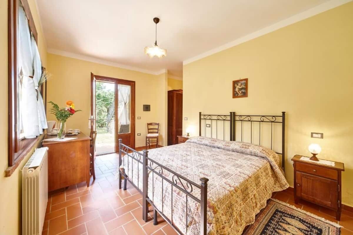 Een slaapkamer met een bed, nachtkastje, raam en een deur die leidt naar een balkon.