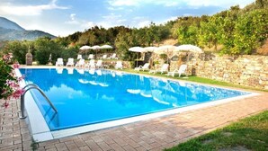 Una piscina con sillones de descanso y sombrillas, rodeada por un muro de piedra y vegetación.